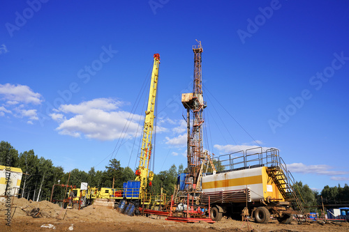 In a row are oil-producing wells. In the background, work is underway to overhaul the well. Drilling rig for drilling oil and gas wells with various equipment and materials.