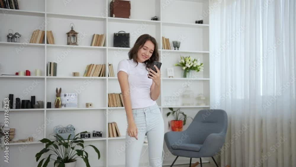 Young girl in white clothes dancing indoors with smartphone in hand. Young girl in white clothes dancing indoors with smartphone in hand.