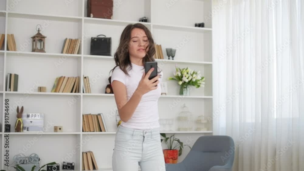 Young girl in white clothes dancing indoors with smartphone in hand. Young girl in white clothes dancing indoors with smartphone in hand.