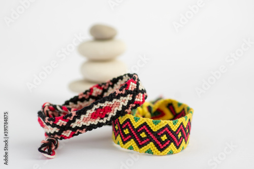 Two handmade homemade colorful natural woven bracelets of friendship with white river stone cairn tower isolated