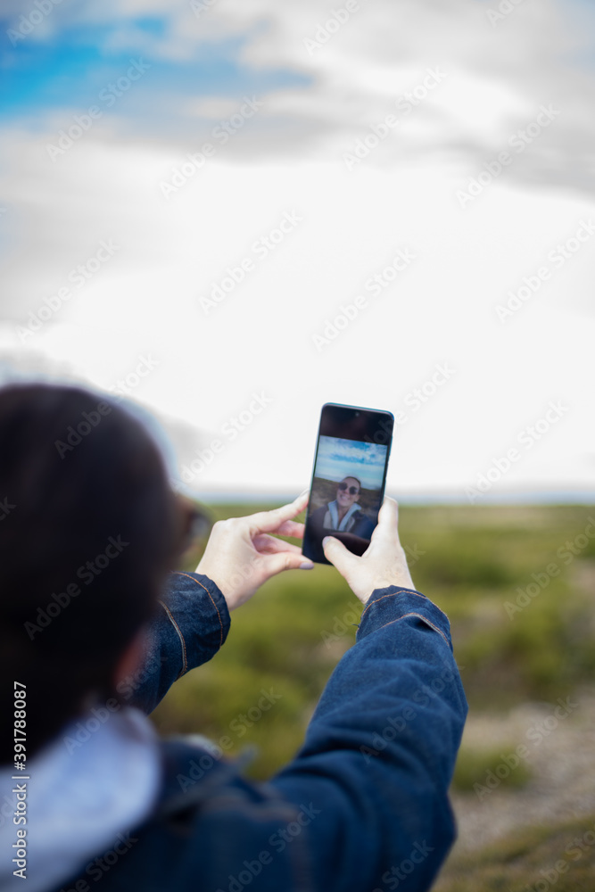 Young woman takes a selfie with her mobile on a mountain surrounded by nature. Woman with sunglasses.