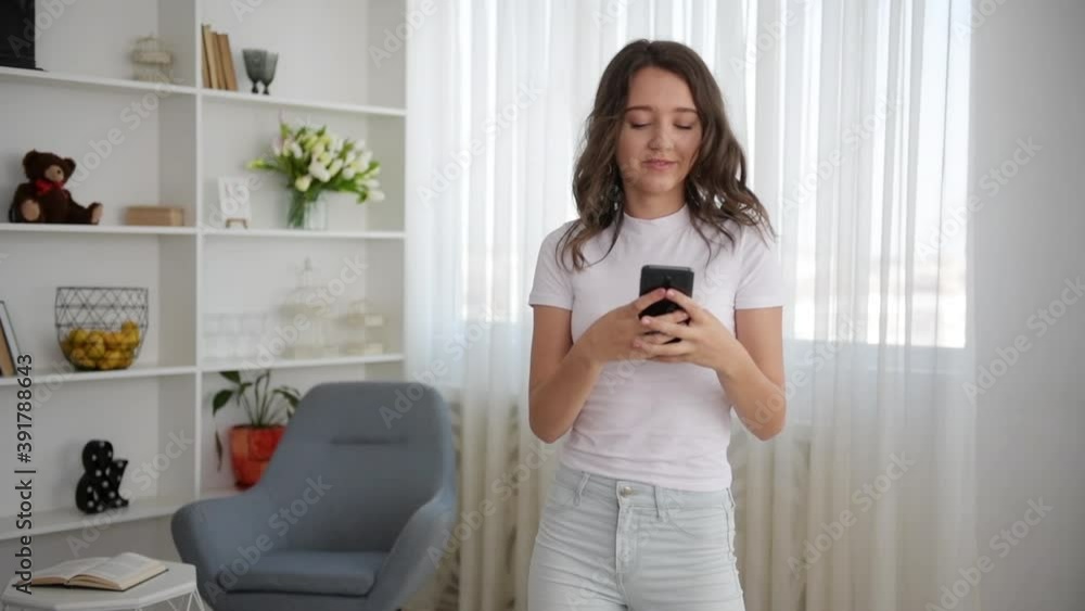 Young girl in white clothes dancing indoors with smartphone in hands. Young girl in white clothes dancing indoors with smartphone in hands.