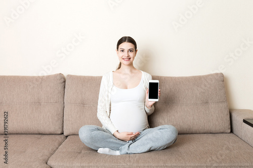 Pregnant woman showing smartphone with black screen in sofa