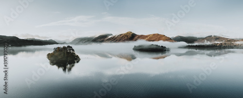 Misty morning on the lake with island reflections and low blue clouds. The Lake District, Cumbria. Autumn colours. 