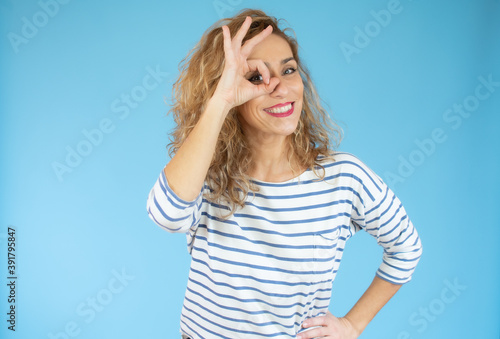 Funny amusing curly woman in striped shirt showing okay gesture near her eye