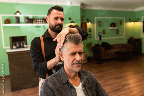 barber combs a man with gray hair and a goatee in a barber shop