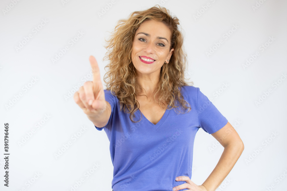 Fototapeta premium Smiling woman in casual clothes pointing up and looking at the camera over white background