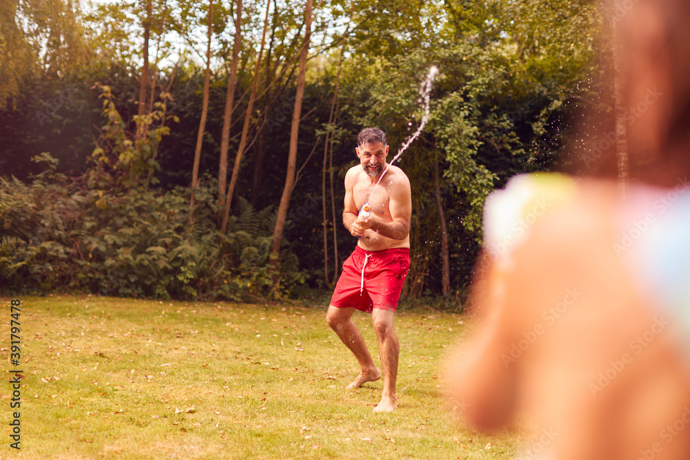 Fototapeta premium Father And Son Wearing Swimming Costumes Having Water Fight With Water Pistols In Summer Garden