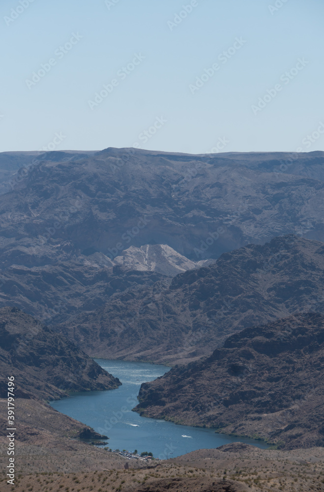 A zoomed in close up of mountains and canyons between Nevada and Arizona show some boats speeding in the river. The desert on a hot summer day can be brutal and recreation near water can be relieving.