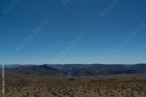 A river can be seen far off in between some mountains and canyons at the border between Arizona and Nevada. The landscape signals proximity close to a famous dam. 