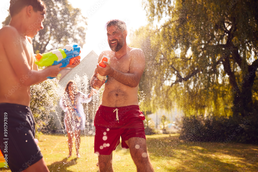 Obraz premium Family Wearing Swimming Costumes Having Water Fight With Water Pistols In Summer Garden