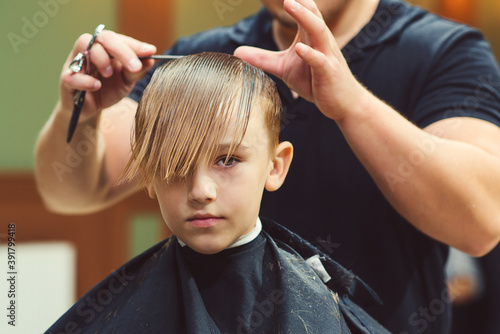 New hairstyle for young boy. Barber shop. Child getting haircut by hairdresser at the barbershop.