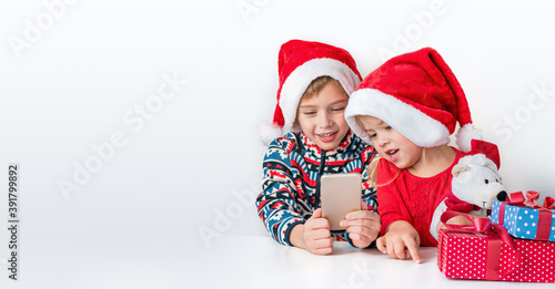 Online christmas greetings. Brother and sister in Santa hats smile and talking on the phone.