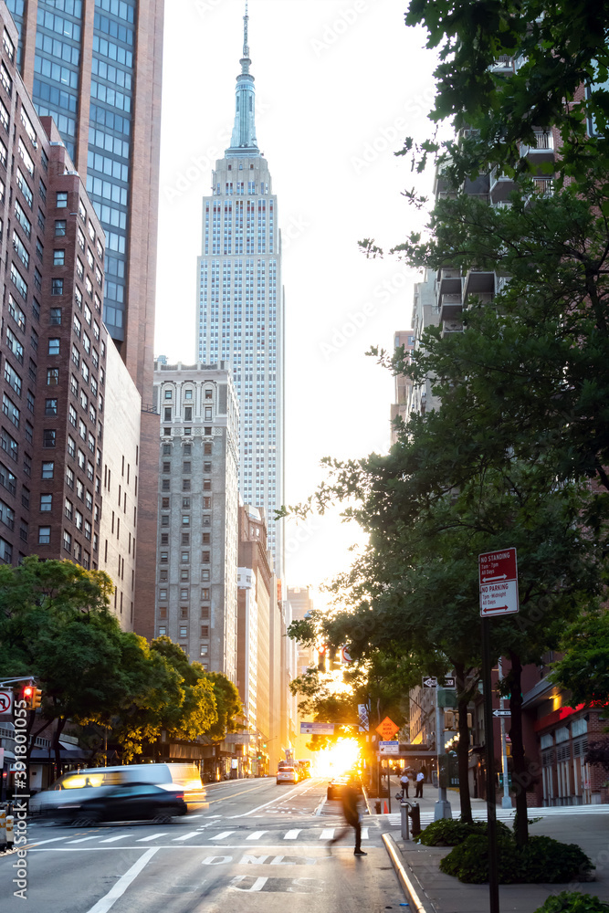 Busy intersection on 42nd Street in Midtown Manhattan with sunset shining between the buildings of the New York City skyline