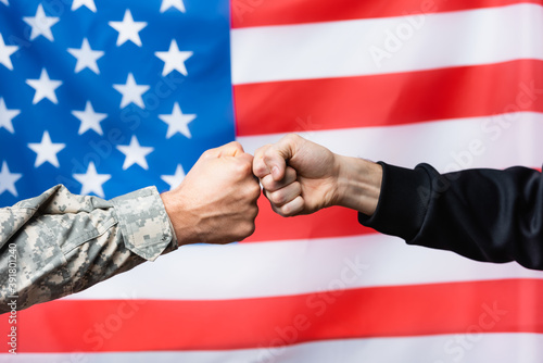 cropped view of soldier fist bumping with civilian man near american flag on blurred background