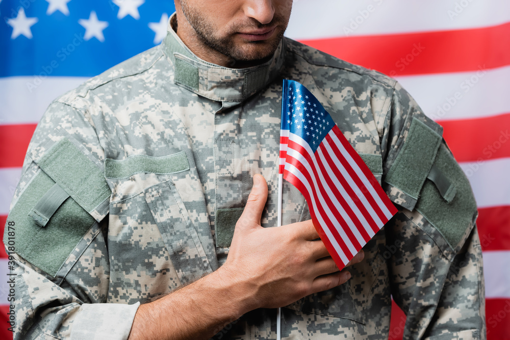 cropped view of patriotic military man in uniform holding small american flag on blurred background cropped view of patriotic military man in uniform holding small american flag on blurred background
