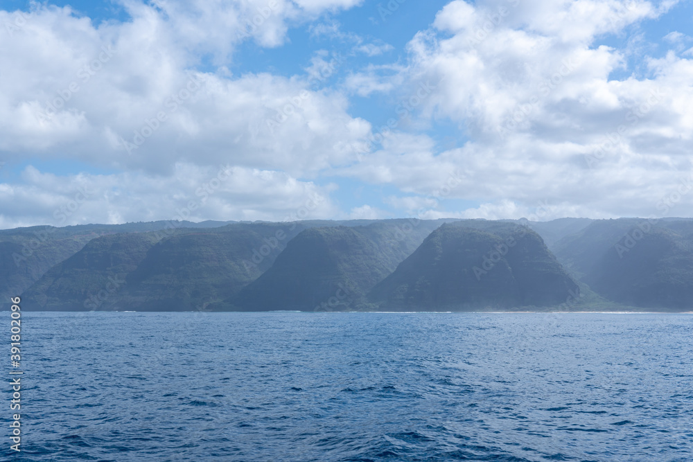 View of a misty Na Pali Coast of the Hawaiian Island, Kaua'i from a boat. The coastline got its name from the obvious towering sea cliffs that rise dramatically over the Pacific Ocean.