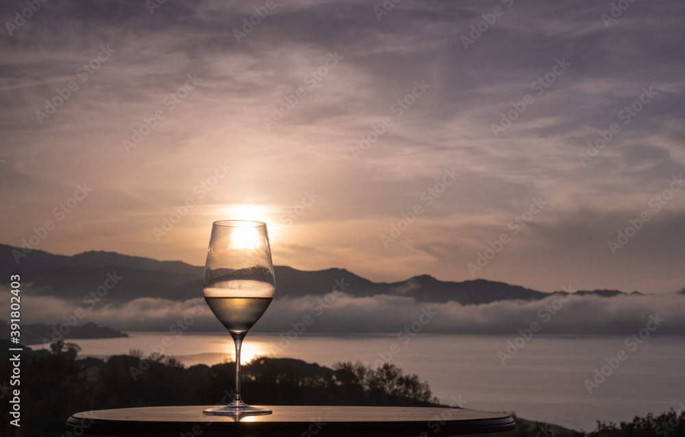 A glass of white Wine with a view over the sea at sunset