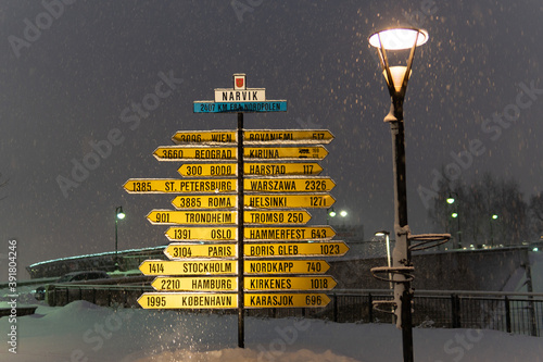 Valokuva Narvik, Norway - December 4, 2019: The famous yellow sign post in the city center lets locals and visitors alike know their distance to other cities and countries, especially the North Pole
