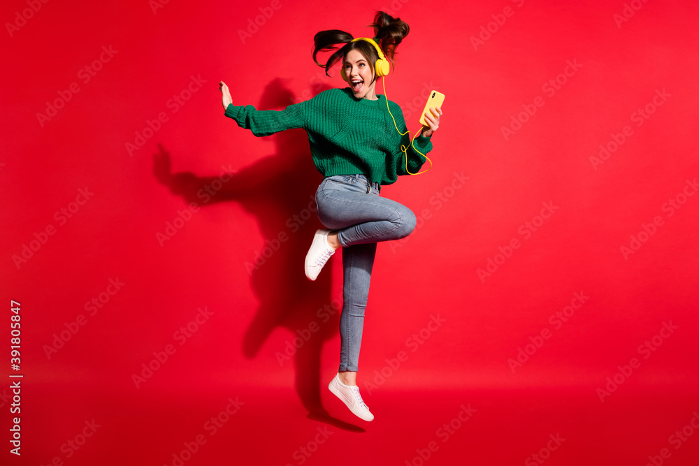 Full length photo of charming young woman dressed green knitted sweater headset dancing jumping isolated red color background