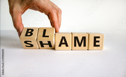 Blame or shame. Male hand flips wooden cubes and changes the inscription 'shame' to 'blame' or vice versa. Beautiful white background, copy space.