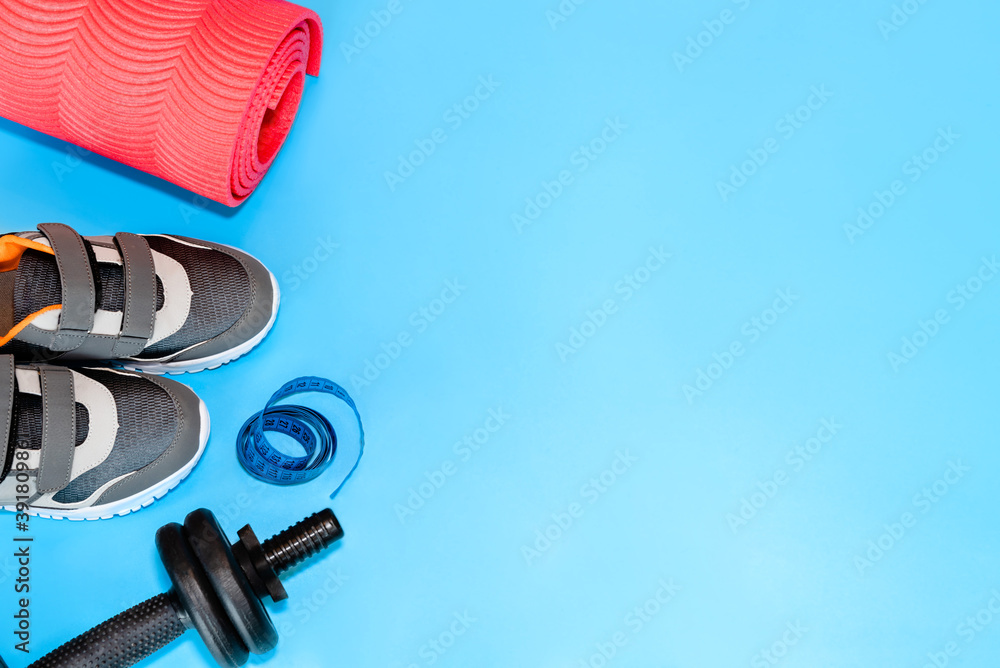 Sports accessories with copy space. Fitness concept set. Sneakers, sports mat, tapeline and dumbbells on blue background. - obrazy, fototapety, plakaty 