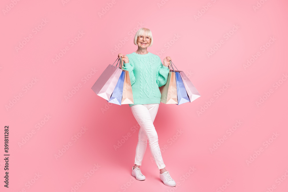 Full length body size photo of happy grandmother keeping bags after sale wearing glasses isolated on pastel pink color background