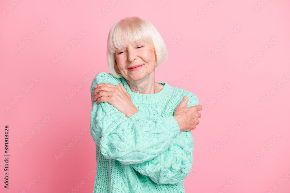 Photo portrait of charming senior woman in turquoise sweater hugging herself closed eyes isolated on pastel pink color background Photo portrait of charming senior woman in turquoise sweater hugging herself closed eyes isolated on pastel pink color background