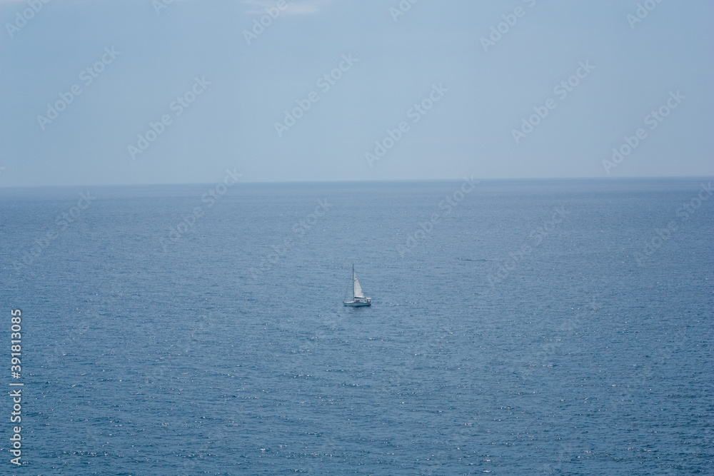 Lonely sailboat in the middle of the blue sea. Clear blue horizon marked.