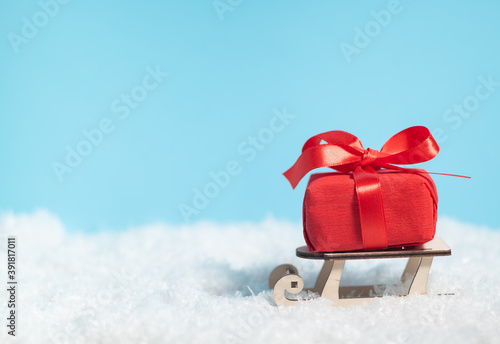 Wooden sleigh delivering Christmas or New Year red present box on blue snowed background