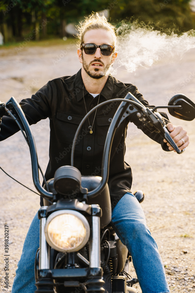 Vertical photo of a young man with sunglasses smoking while riding a motorcycle