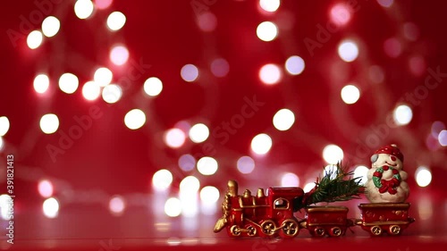 Christmas toy train with a snowman and a Christmas tree moves against a background of red color and a sparkling garland
