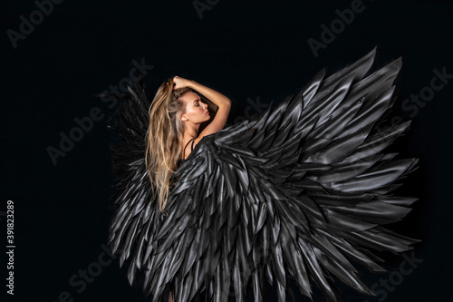 beautiful blonde girl in a black suit with black wings on a black background