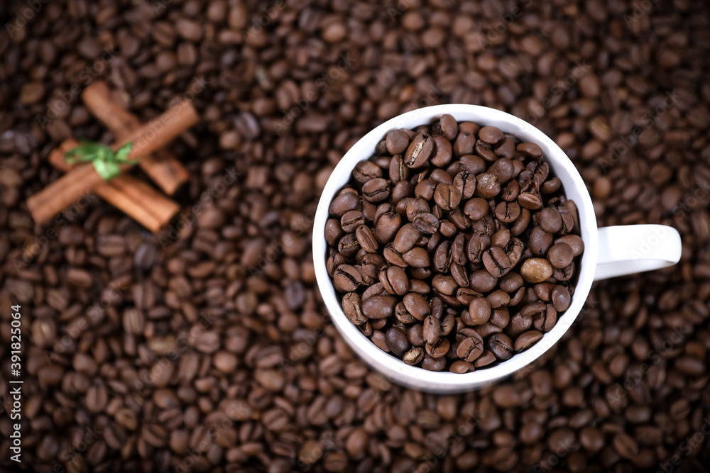 Fototapeta premium White cup full of coffee beans and cinnamon on a coffee beans background. Coffee mug. 