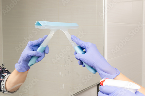closeup female hands sprinkle cleaning agent on the bathroom mirror and wipe it