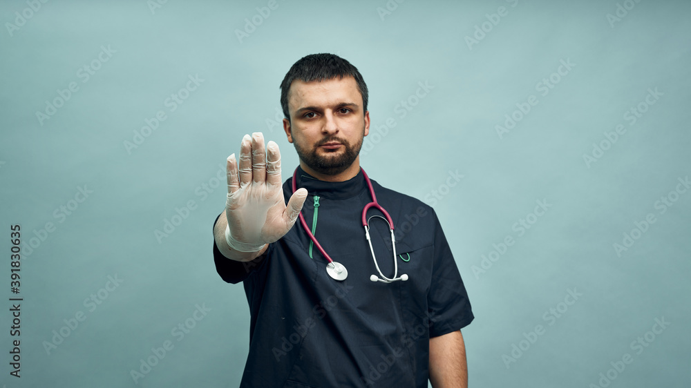 The doctor extends a gloved hand to the camera. Stop sign. Keeping distance in a pandemic. Personal protective equipment. The doctor extends a gloved hand to the camera. Stop sign. Keeping distance in a pandemic. Personal protective equipment.