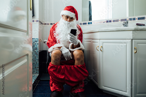 Santa Claus in the bathroom, sitting on the toilet pooping and looking at his cell phone