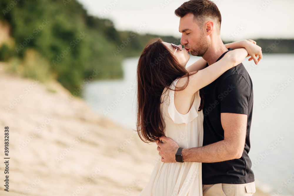 Romantic couple is kissing outdoors. elegant and stylish woman and man in love are walking along the lake. Happy moments together. love story