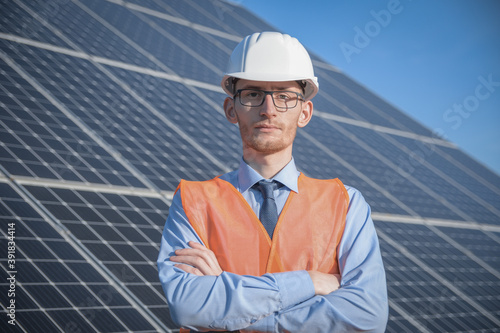 Engineer, man in uniform, helmet glasses and work jacket on a background of solar panels at solar station. Technician check the maintenance. © Ivan