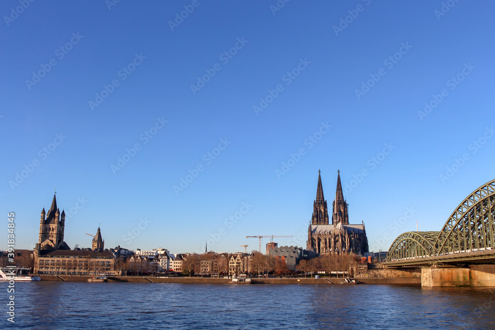 View of Cologne with the Great St. Martin Church, the Cologne Cathedral (Kolner Dom) and Hohenzollern Bridge from bank of the Rhine river, Germany.