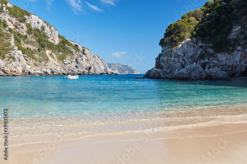 Empty beach of Agios Spyridon bay in Corfu island in Greece, surrounded by rocks on a sunny holiday day. At sea, you can see a motorboat with tourists.