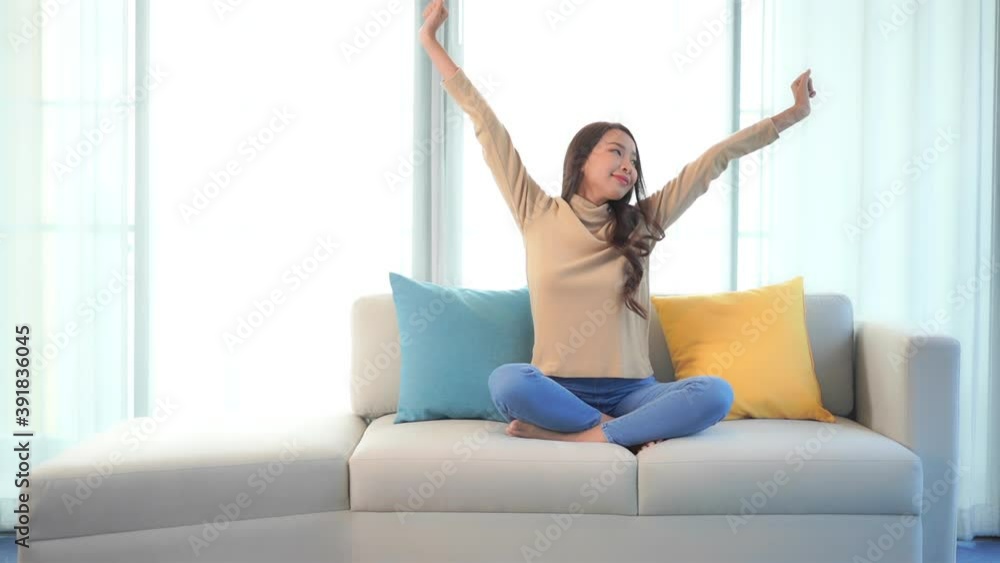 Asian woman stretching her arms sitting on sofa at home near window. Asian woman stretching her arms sitting on sofa at home near window.
