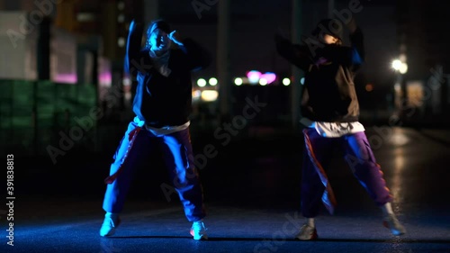 Two energetic young women dancing hip hop, freestyle at night on a city street in the light of lanterns.
