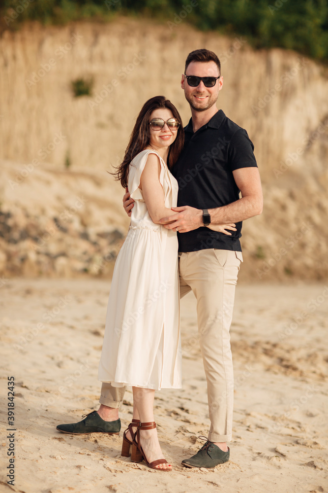 Happy lovers at the beach near lake. Young couple is hugging at sunset on summer day outdoors. A man and woman in love. Concept of love and family. full length. Close Up. Happy lovers at the beach near lake. Young couple is hugging at sunset on summer day outdoors. A man and woman in love. Concept of love and family. full length. Close Up.