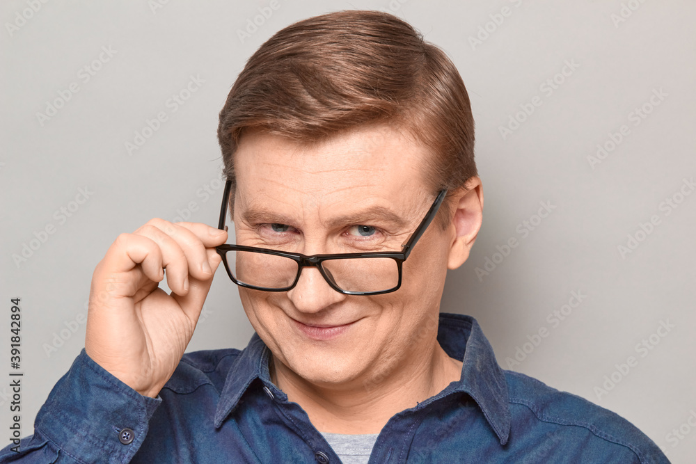 Portrait of happy blond mature man looking over his glasses at you