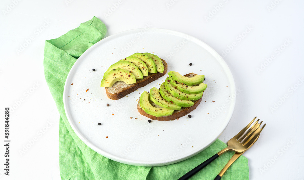 Diet sandwiches in a white plate on a light background. Slices of fresh avocado on bread. The concept of natural products.