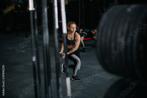 Sporty young woman with perfect athletic body wearing black sportswear working out with kettlebell during sport workout training at modern fitness gym with dark interior.