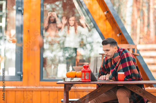 Happy young man working on laptop and drinking coffee sitting at the wooden table outdoors