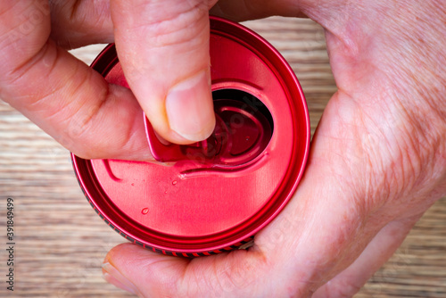 Manos abren una lata de aluminio rojo, de bebida refrescante, visto desde arriba