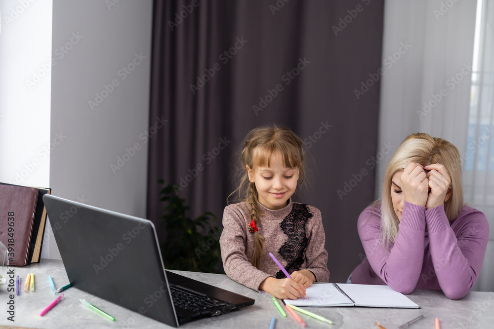 Woman helping young girl with laptop do homework in dining room